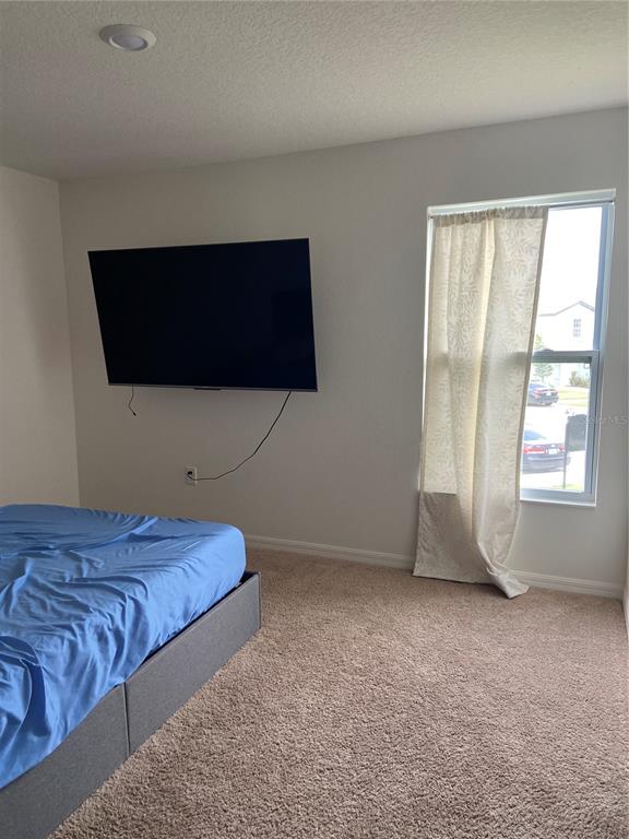 A bedroom features a wall-mounted television, a bed with blue bedding, and a window — 1523 WYNFORD CIRCLE, TAVARES, FL