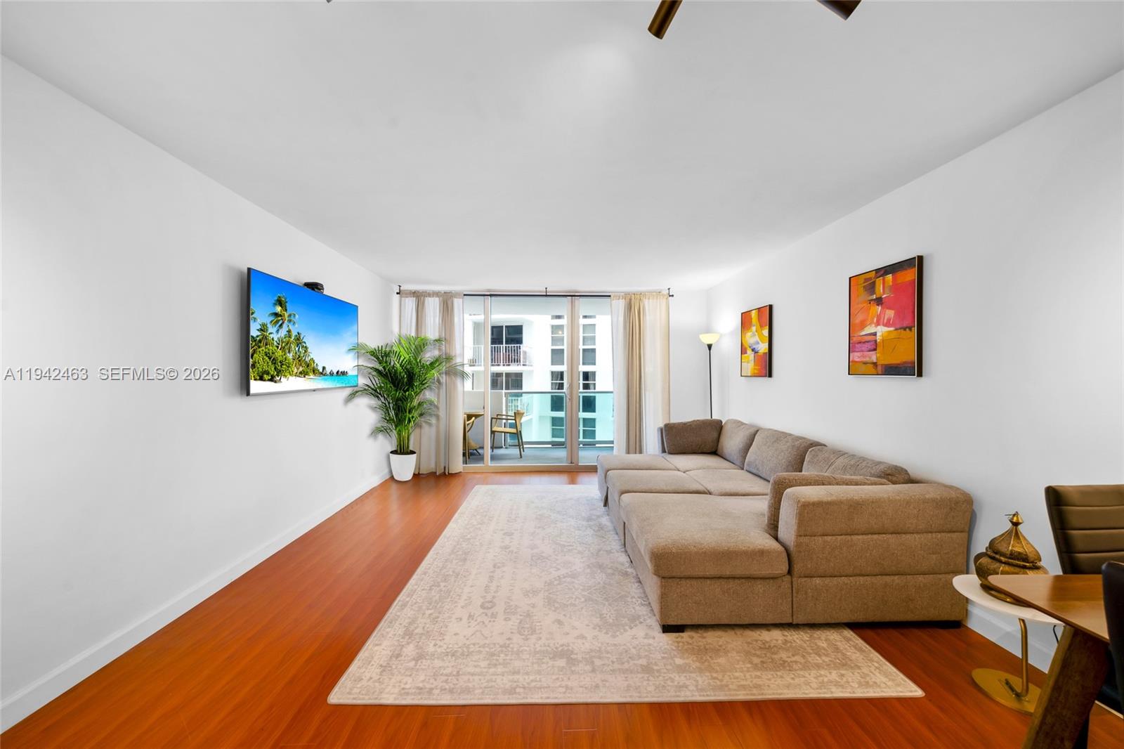 A living room features wood flooring, a sectional sofa, a wall-mounted television, and a balcony — 1200 West Ave # 422, Miami Beach FL 33139, MIAMI BEACH, FL