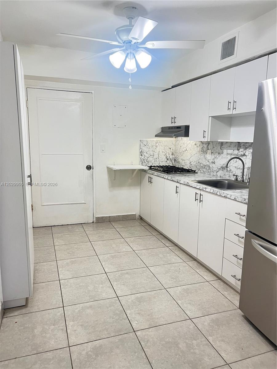 A kitchen features white cabinets, marble-patterned countertops, stainless steel appliances, and light-colored floor tiles — 1401 E 8th Ave, Hialeah FL 33010, HIALEAH, FL