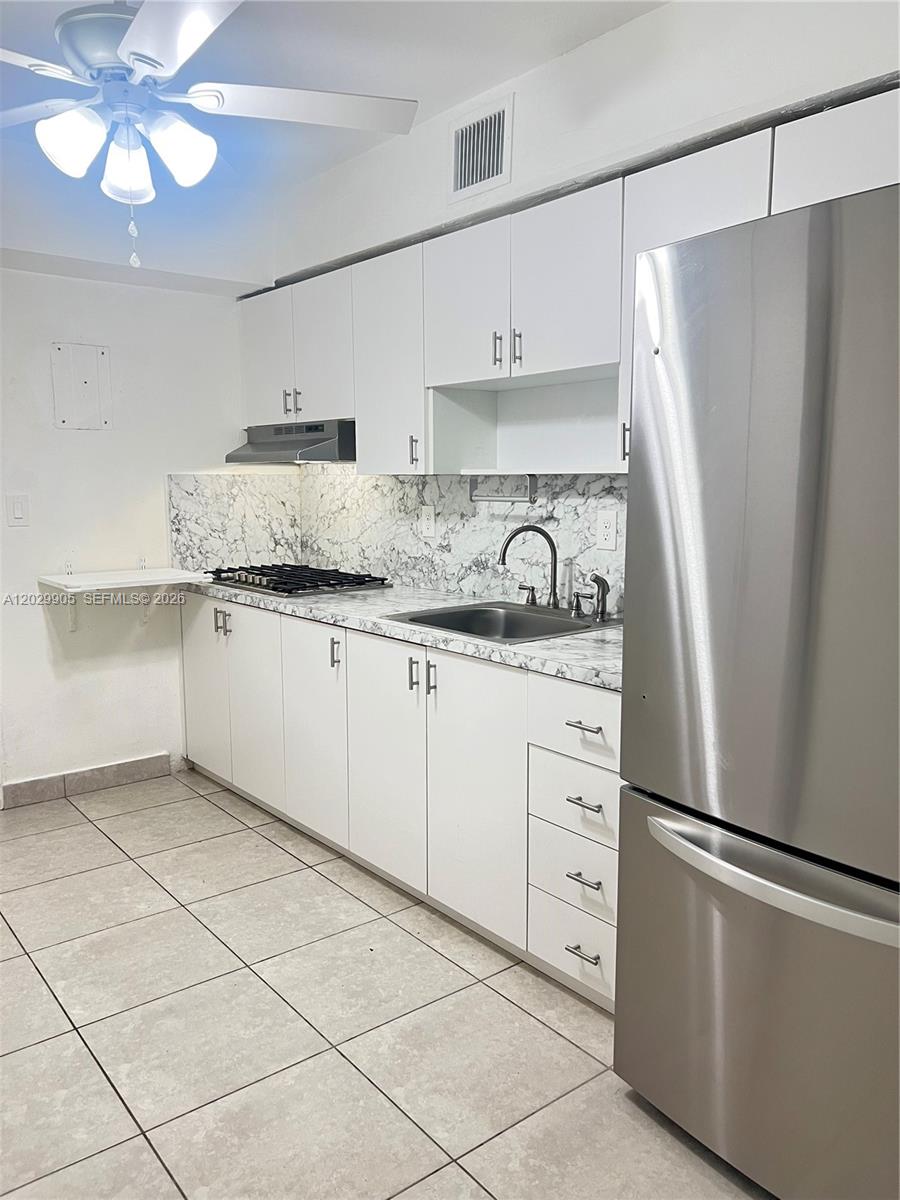A kitchen features white cabinets, marble-patterned countertops, a stainless steel refrigerator, and tiled flooring — 1401 E 8th Ave, Hialeah FL 33010, HIALEAH, FL