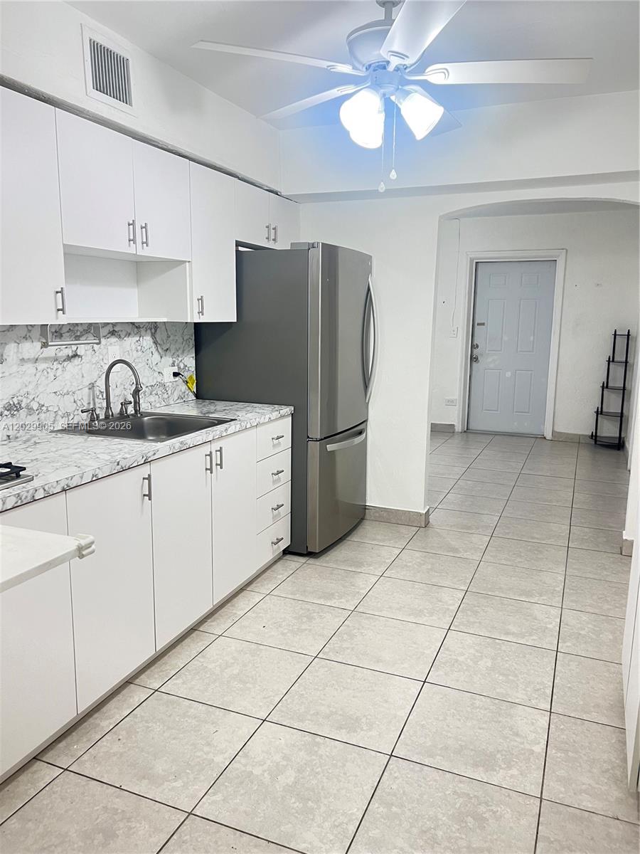 A kitchen features white cabinets, a stainless steel refrigerator, and marble-patterned countertops — 1401 E 8th Ave, Hialeah FL 33010, HIALEAH, FL