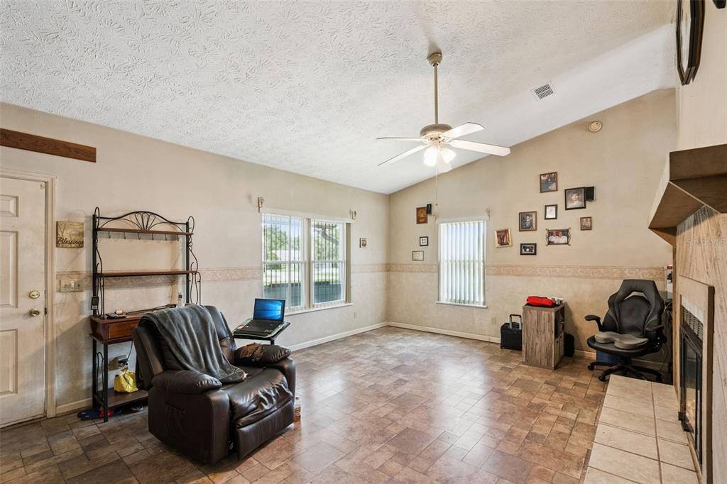A living room features tile flooring, a vaulted ceiling with a fan, and a fireplace — 1869 KINGS POINT BOULEVARD, KISSIMMEE, FL