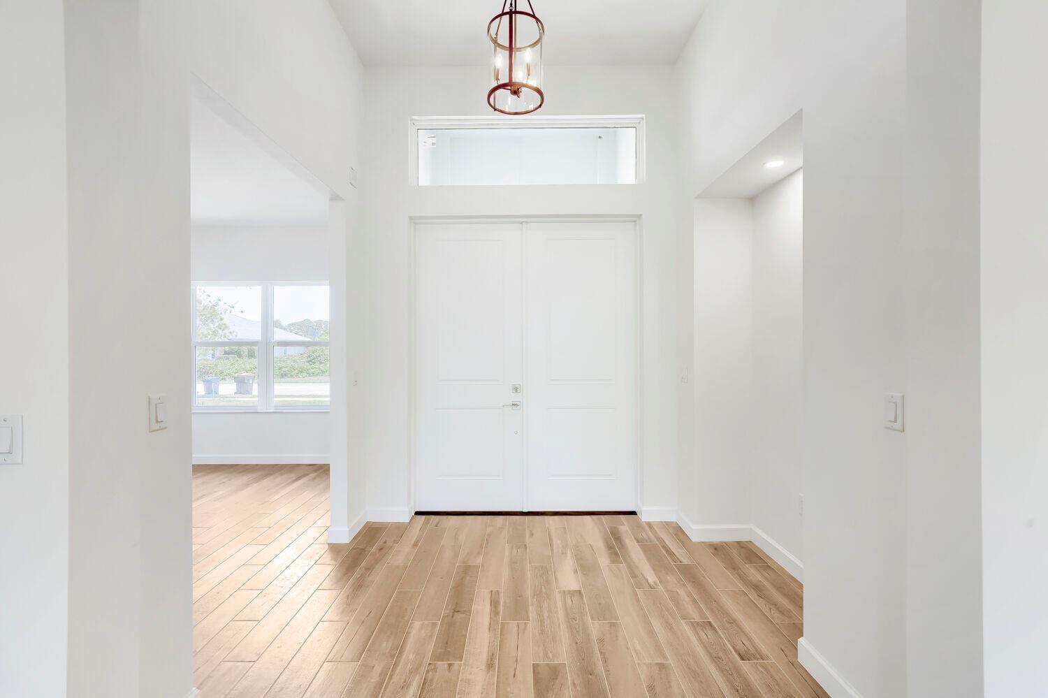 A bright entryway features white double doors, light wood flooring, and a modern pendant light — 6635 49th Court, Vero Beach FL 32967, VERO BEACH, FL