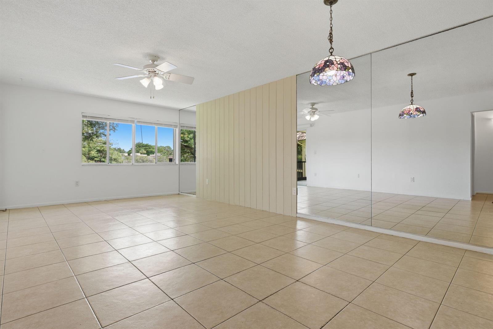 An empty room features beige tile flooring, a ceiling fan, a paneled wall, and mirrored walls — 824 SW 9th Street Circle # 201, Boca Raton FL 33486, BOCA RATON, FL