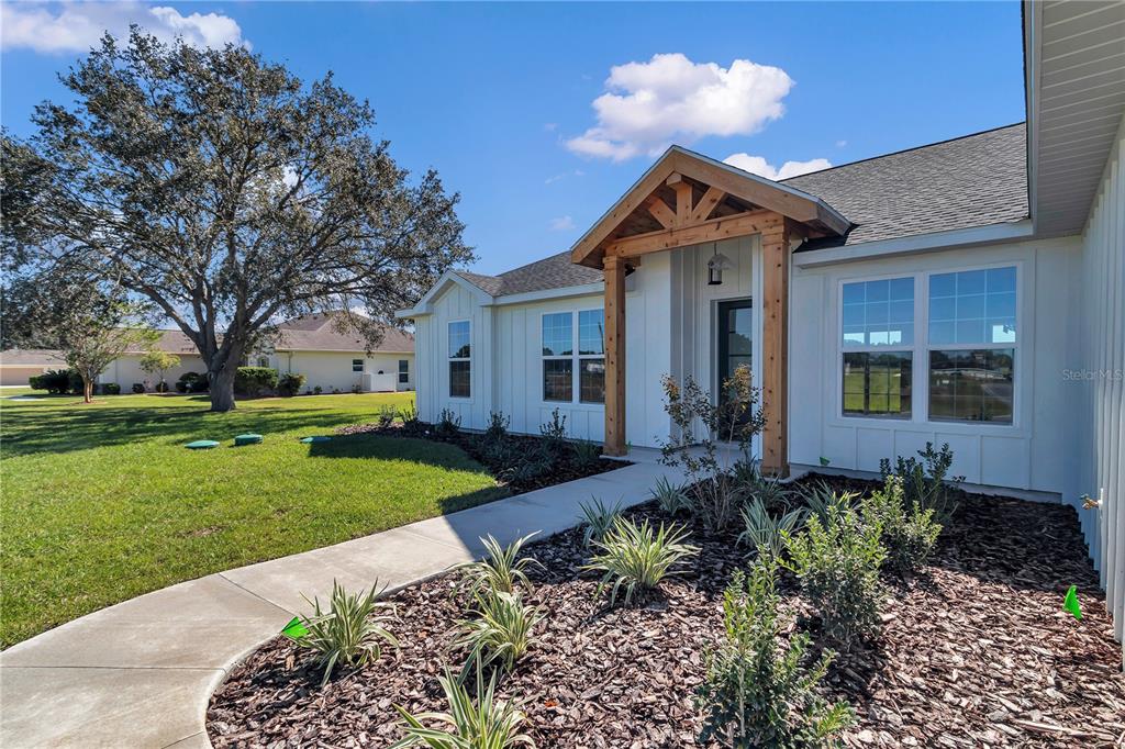 A white house exterior features a wooden porch gable, a concrete walkway, and landscaped mulch — 1916 NW 80TH STREET, OCALA, FL