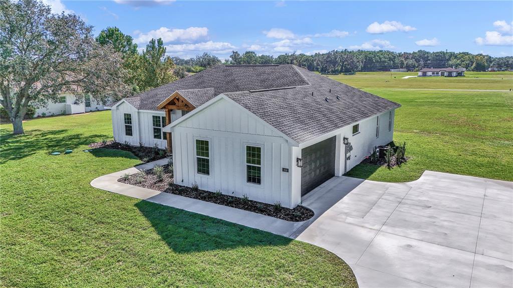 An aerial view of a white farmhouse-style home with a dark roof and concrete driveway — 1916 NW 80TH STREET, OCALA, FL