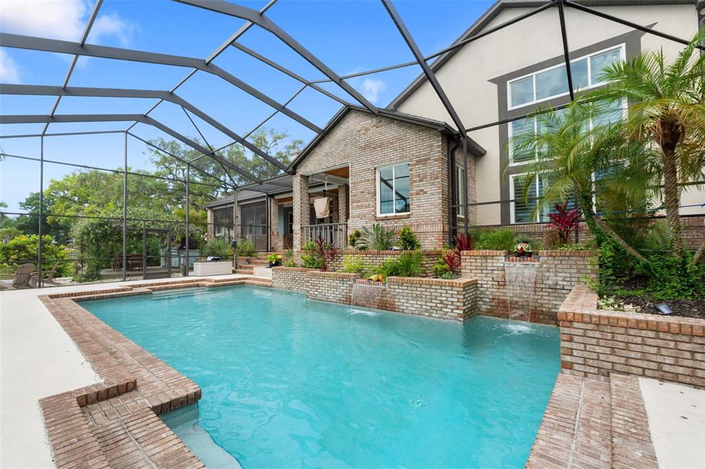 A swimming pool with two water features sits inside a screened-in patio by a house — 6936 RIVER ROAD, NEW PORT RICHEY, FL