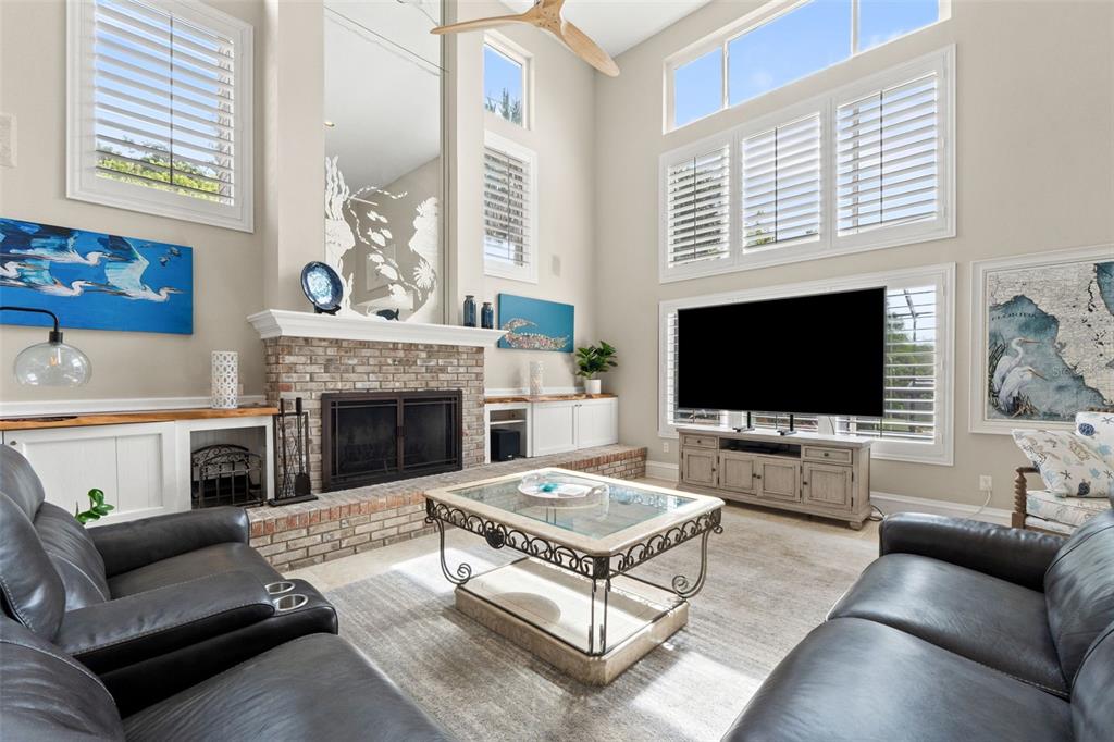 A living room features a brick fireplace, a large television, and high ceilings with windows — 6936 RIVER ROAD, NEW PORT RICHEY, FL