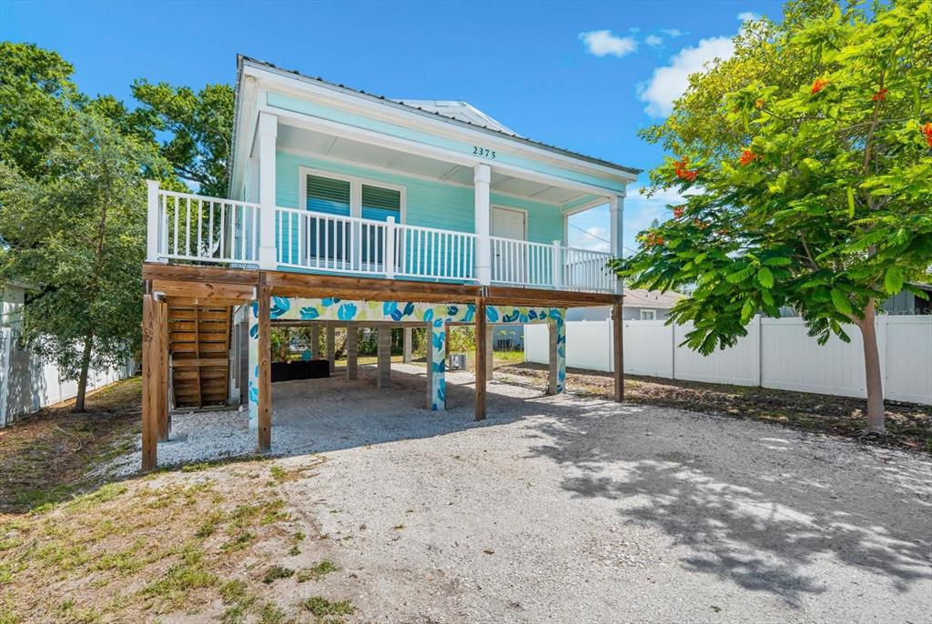 A light blue elevated house with a white porch and gravel driveway under the structure — 2375 BAHIA VISTA STREET, SARASOTA, FL