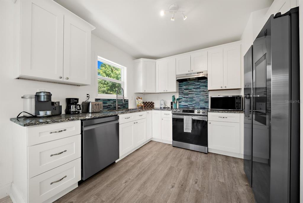 A kitchen features white cabinets, granite countertops, stainless steel appliances, and a blue tile backsplash — 2375 BAHIA VISTA STREET, SARASOTA, FL