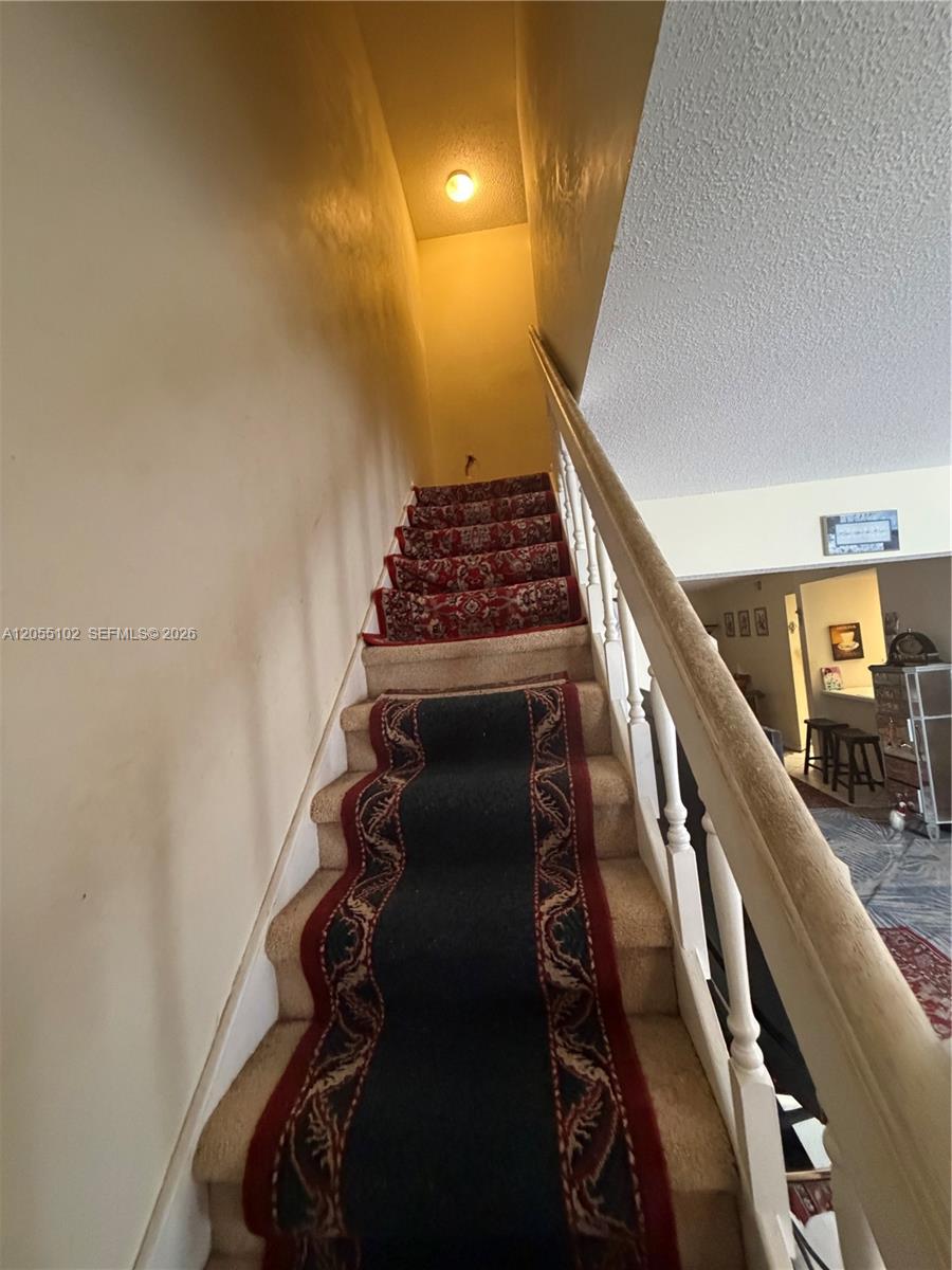 A staircase with a patterned runner leads upward between a plain wall and a railing — 1727 NW 80th Ave # H, Margate FL 33063, MARGATE, FL