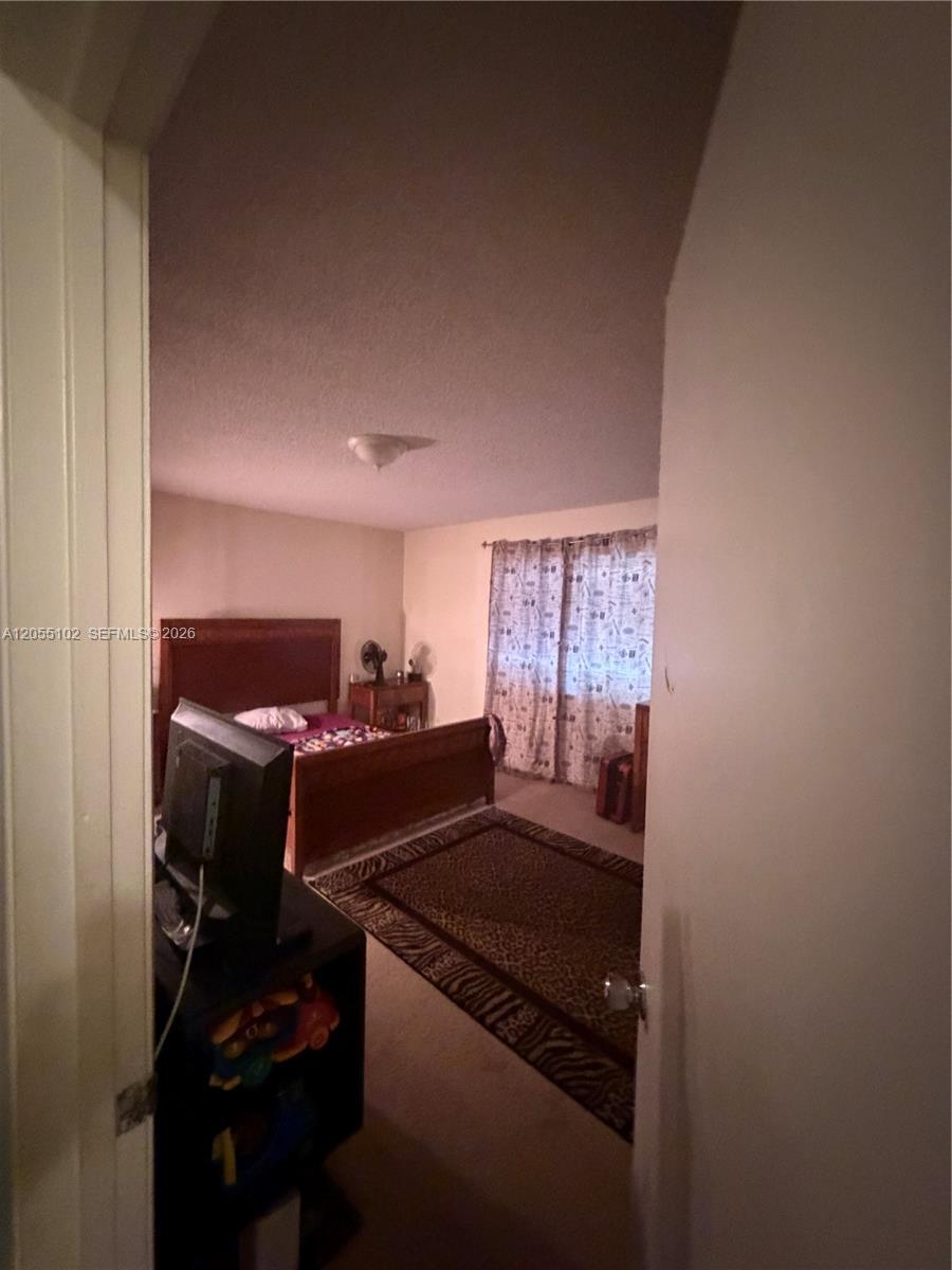 A bedroom features a wooden bed frame, a patterned area rug, and a window with curtains — 1727 NW 80th Ave # H, Margate FL 33063, MARGATE, FL