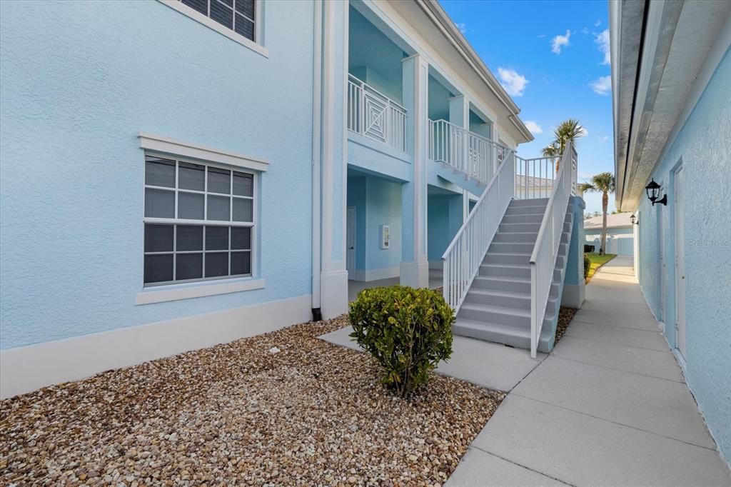 A light blue two-story building features an exterior staircase leading to an upper balcony — 5747 SABAL TRACE DRIVE UNIT 203, NORTH PORT, FL