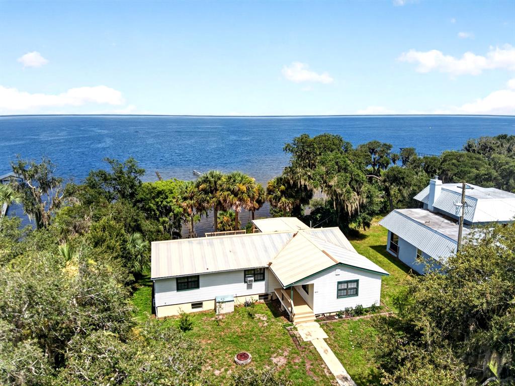 An aerial view shows a white house with a metal roof near a large lake — 8445 NE 310TH AVENUE, FORT MC COY, FL