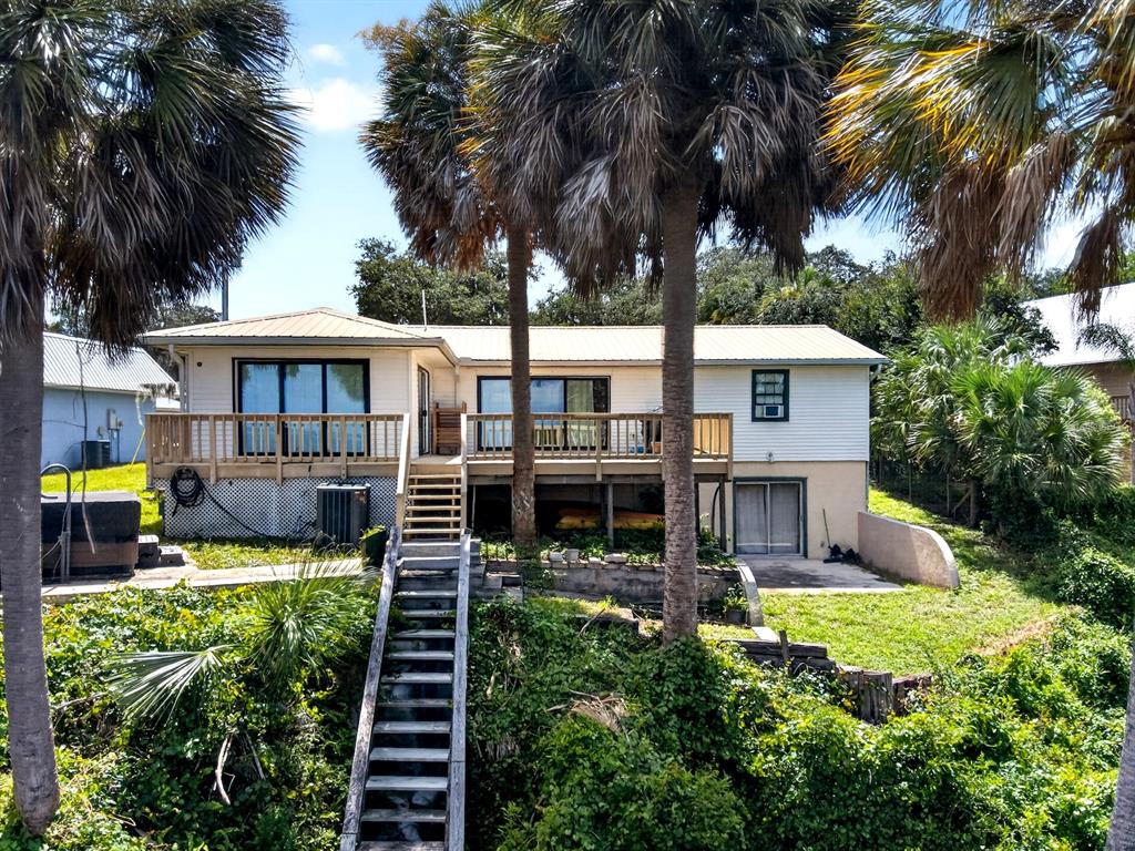 A raised house with a wooden deck, stairs, and palm trees in a grassy yard — 8445 NE 310TH AVENUE, FORT MC COY, FL