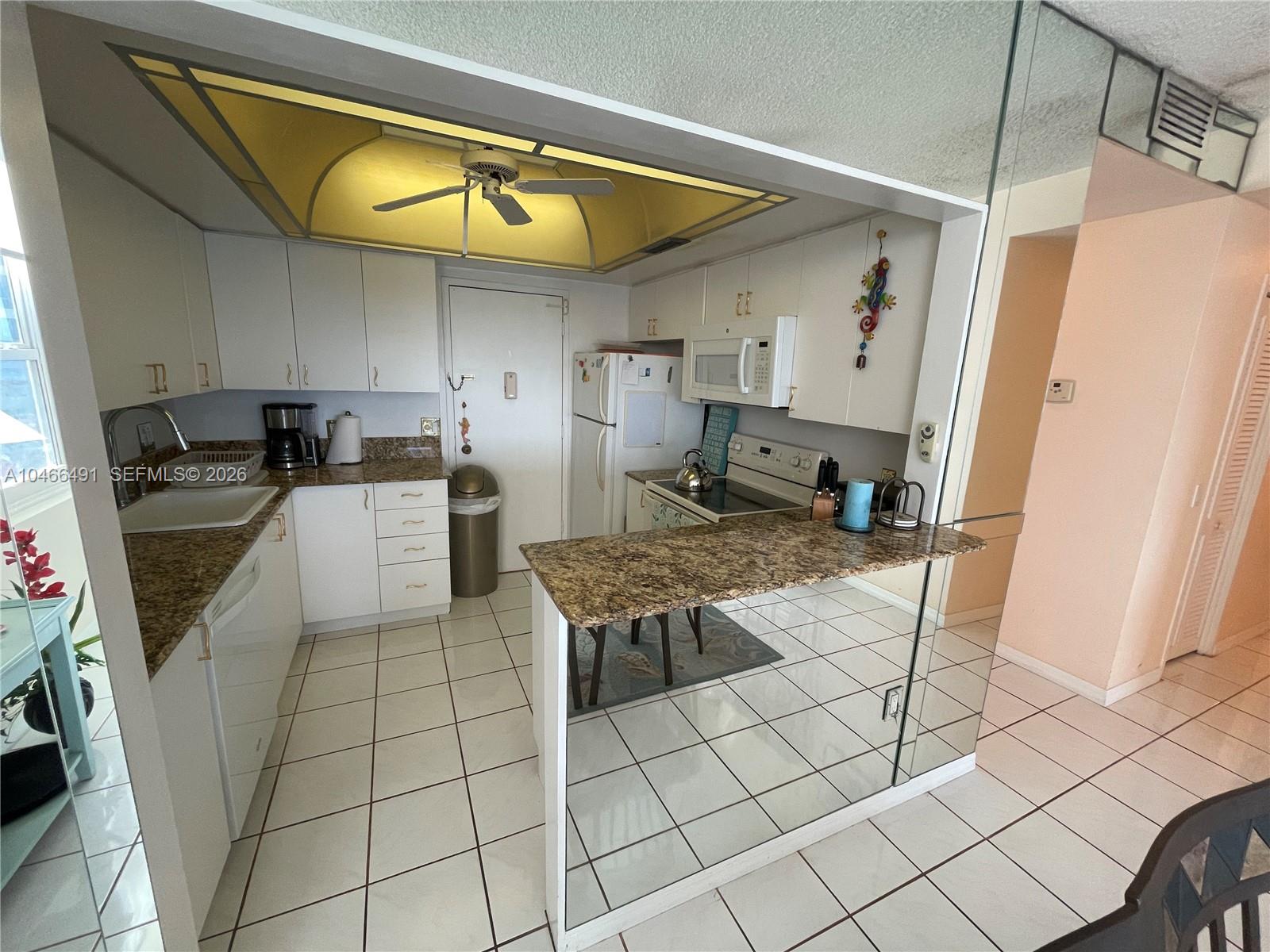 A kitchen features white cabinets, granite countertops, a mirrored breakfast bar, and tiled flooring — 3505 S OCEAN DR # 421, Hollywood FL 33019, HOLLYWOOD, FL