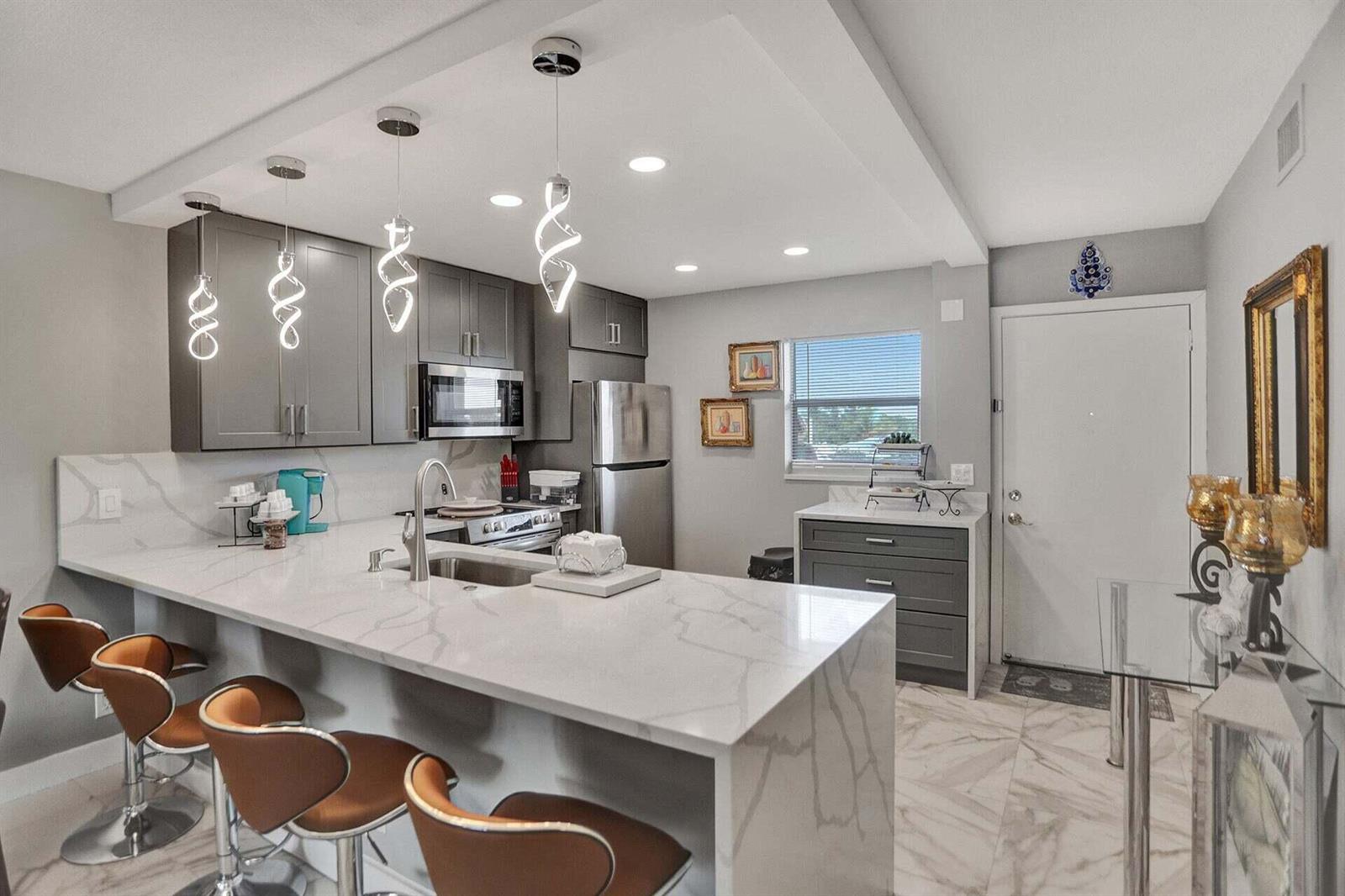 A modern kitchen features gray cabinets, a white marble waterfall island, and three pendant lights — 130 NE 26th Avenue # 3070, Boynton Beach FL 33435, BOYNTON BEACH, FL