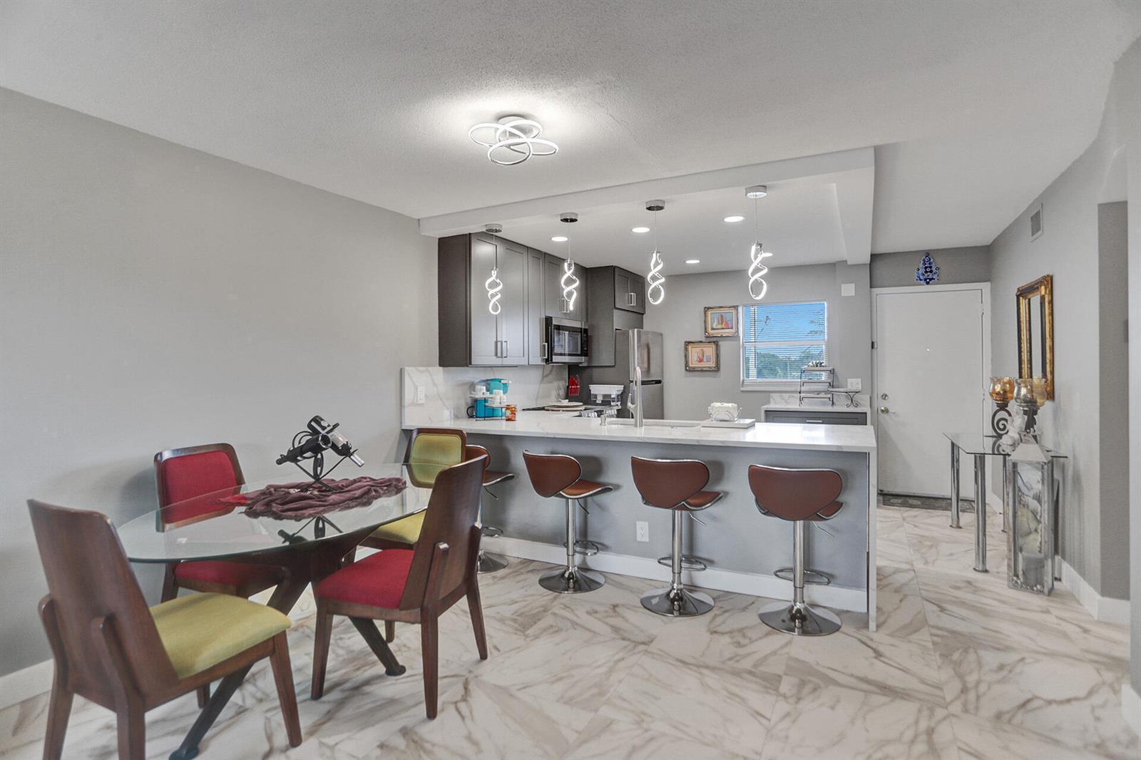 An open-concept kitchen and dining area features a glass-top table, bar seating, and marble flooring — 130 NE 26th Avenue # 3070, Boynton Beach FL 33435, BOYNTON BEACH, FL