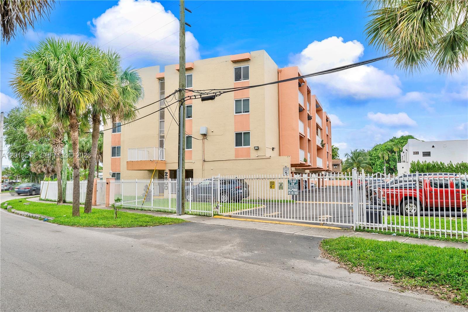 A multi-story apartment building features a white fence, palm trees, and a parking area — 2400 NW 16th St Rd, Miami FL 33125, MIAMI, FL