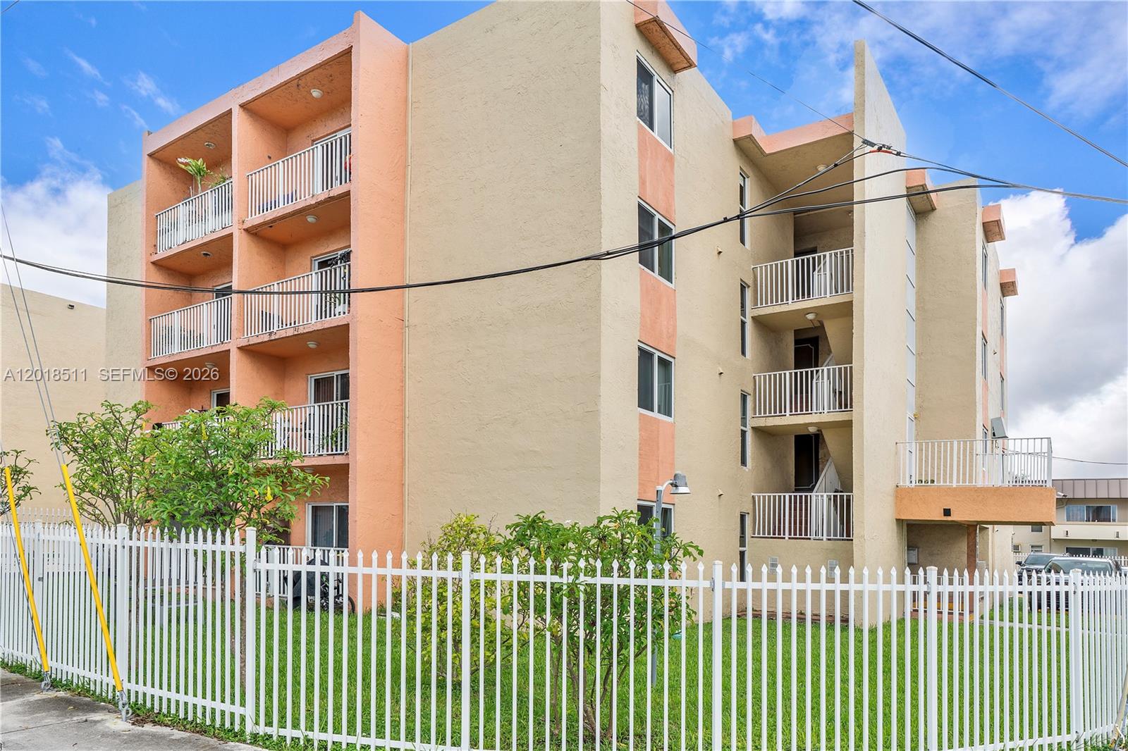 A multi-story apartment building with peach-colored accents and white balconies behind a white fence — 2400 NW 16th St Rd, Miami FL 33125, MIAMI, FL