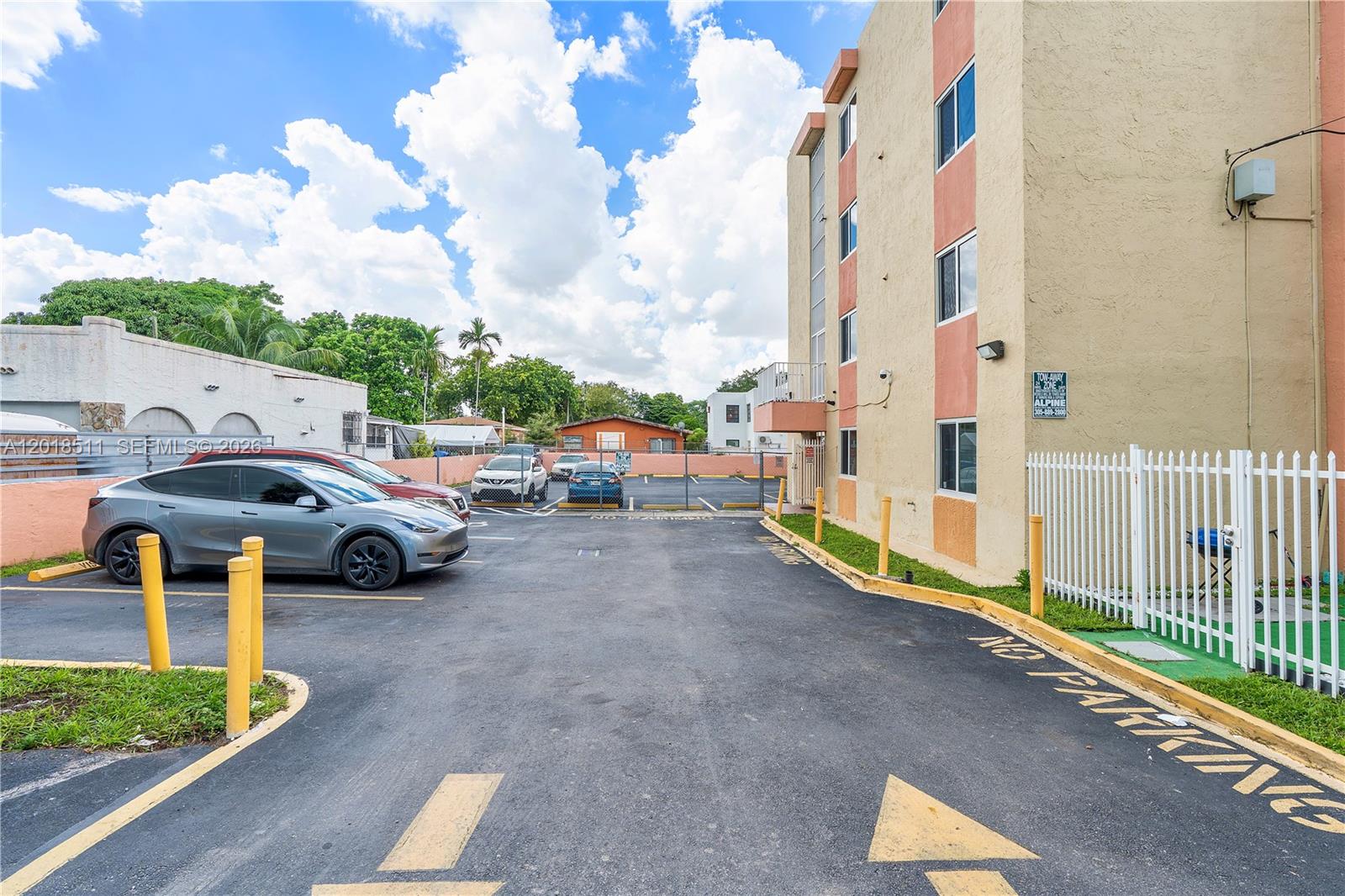 A paved parking lot sits beside a multi-story apartment building under a cloudy blue sky — 2400 NW 16th St Rd, Miami FL 33125, MIAMI, FL