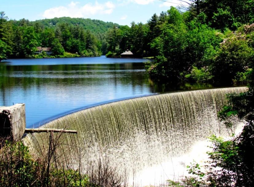 A curved dam spills water into a lake surrounded by lush green trees and hills — 15xx FRANKLIN ROAD, HIGHLANDS, NC