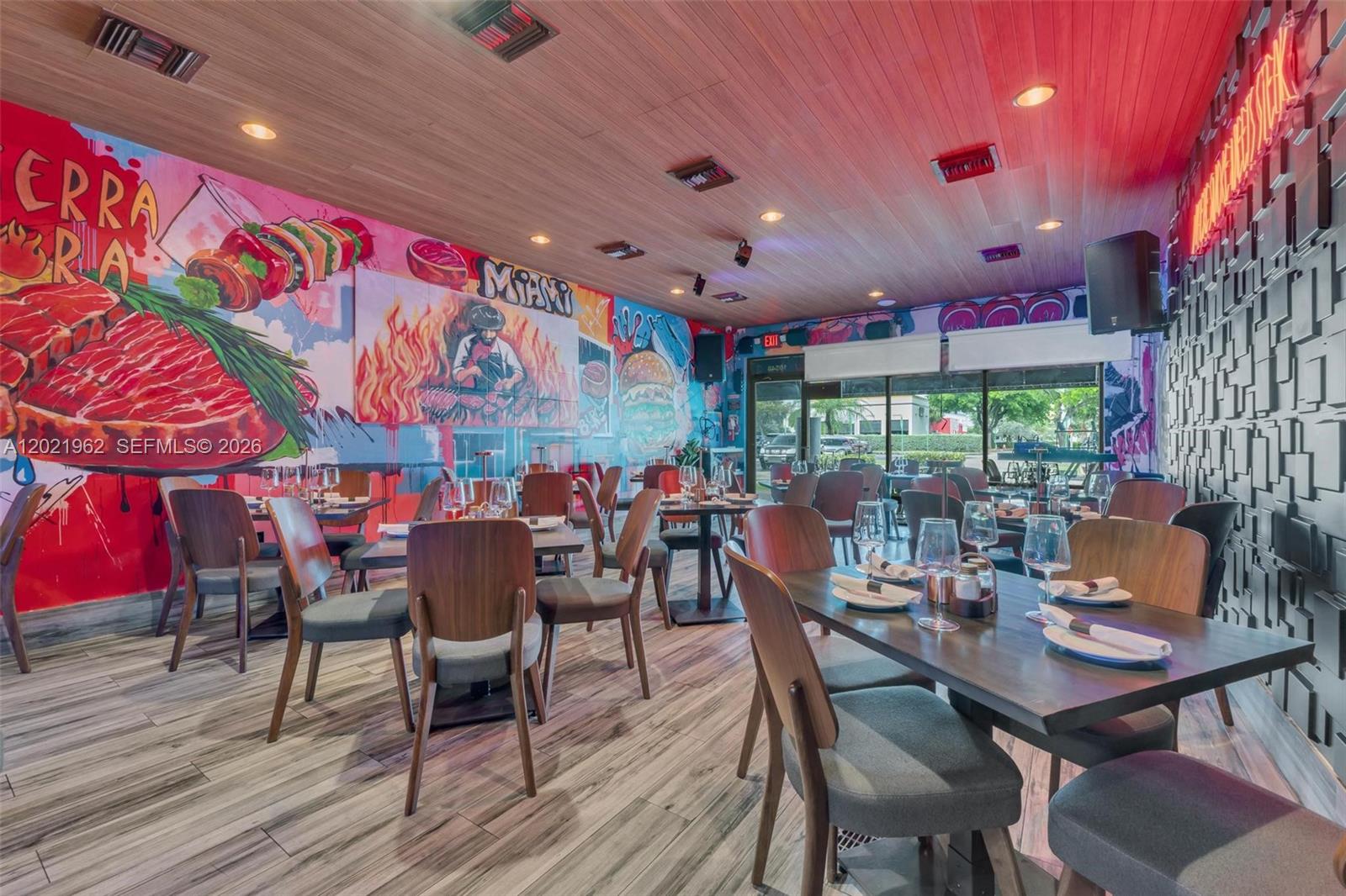 A restaurant dining room features wood-paneled ceilings, a vibrant mural, and modern wooden furniture — 10548 SW 8, Miami FL 33174, MIAMI, FL