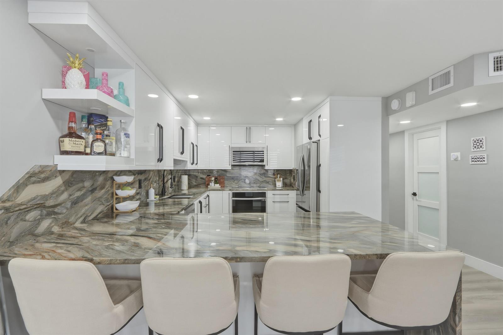 A modern kitchen features white cabinets, a marble countertop island, and four cream-colored bar stools — 6039 Collins Avenue # 609, Miami Beach FL 33140, MIAMI BEACH, FL
