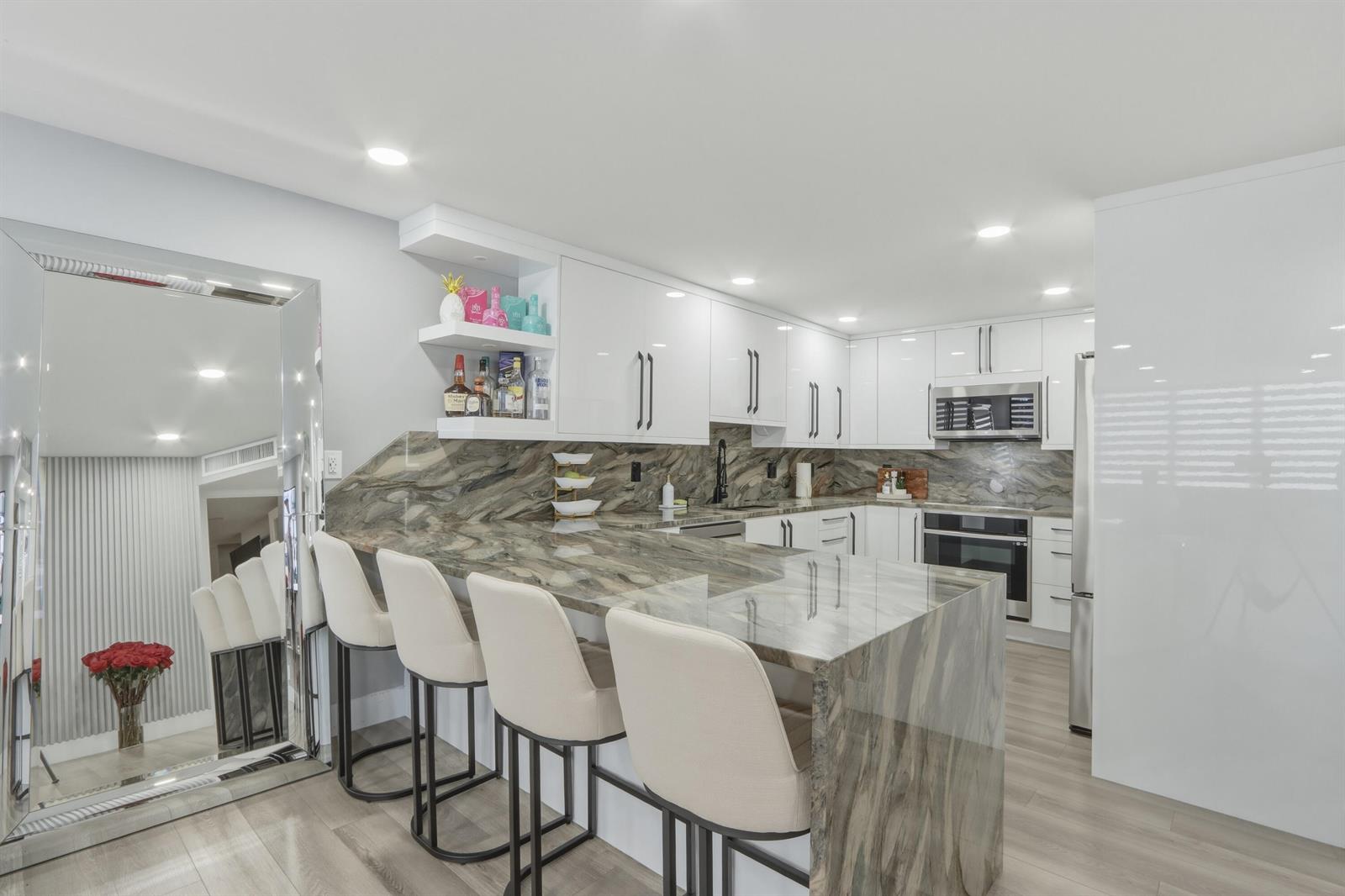 A modern kitchen features white cabinets, a waterfall stone island, and four bar stools — 6039 Collins Avenue # 609, Miami Beach FL 33140, MIAMI BEACH, FL