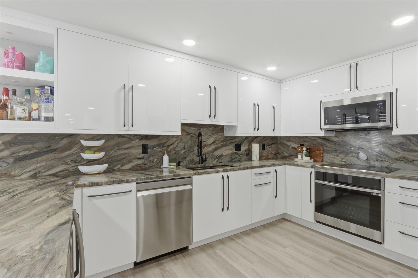 A modern kitchen features white cabinets, stainless steel appliances, and a dramatic brown stone backsplash — 6039 Collins Avenue # 609, Miami Beach FL 33140, MIAMI BEACH, FL