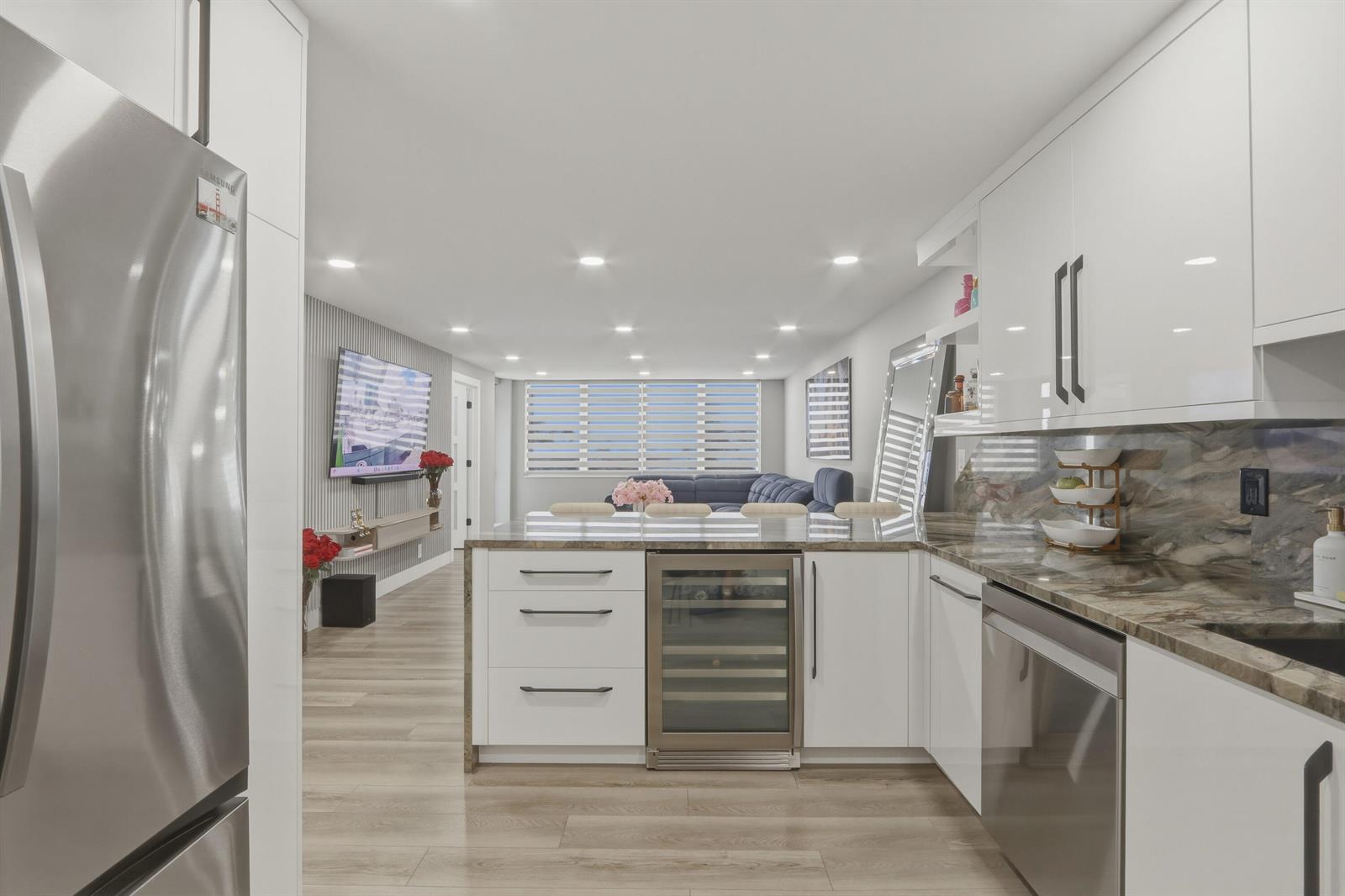 A modern kitchen with white cabinetry and marble countertops opens into a living area — 6039 Collins Avenue # 609, Miami Beach FL 33140, MIAMI BEACH, FL