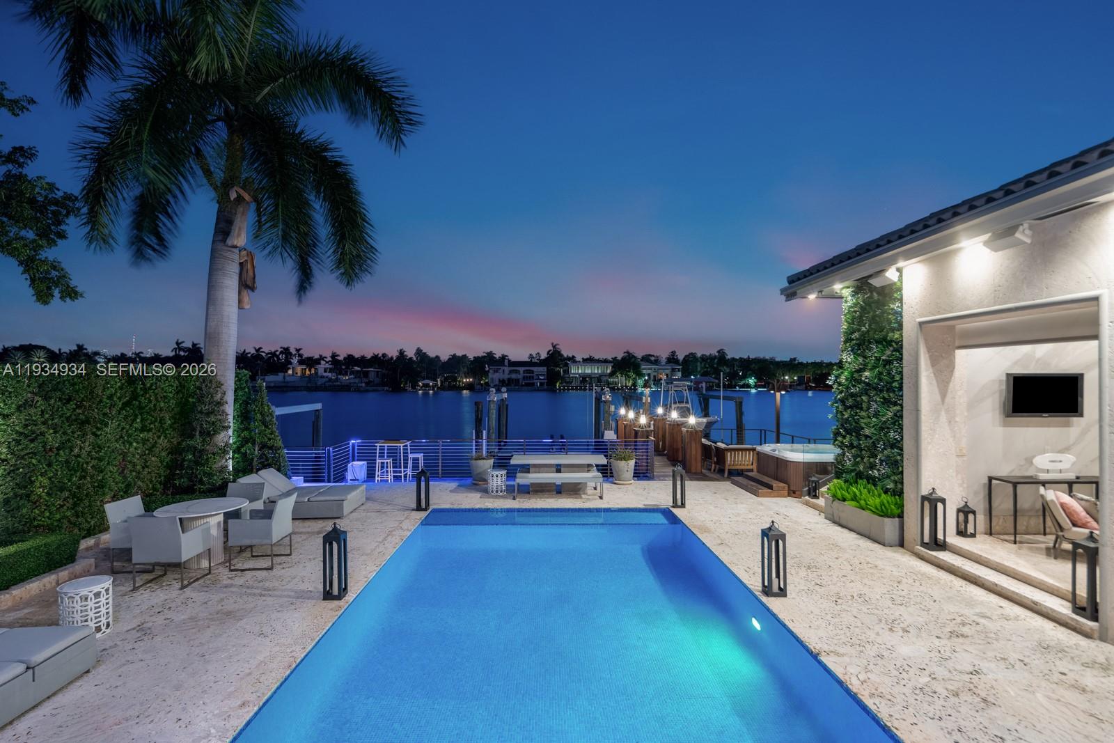 A swimming pool sits on a stone patio overlooking a canal at twilight — 176 S Hibiscus Drive, Miami Beach FL 33139, MIAMI BEACH, FL