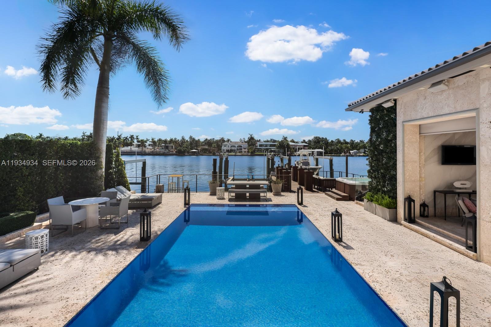 A rectangular swimming pool sits on a stone patio overlooking a canal and boat dock — 176 S Hibiscus Drive, Miami Beach FL 33139, MIAMI BEACH, FL