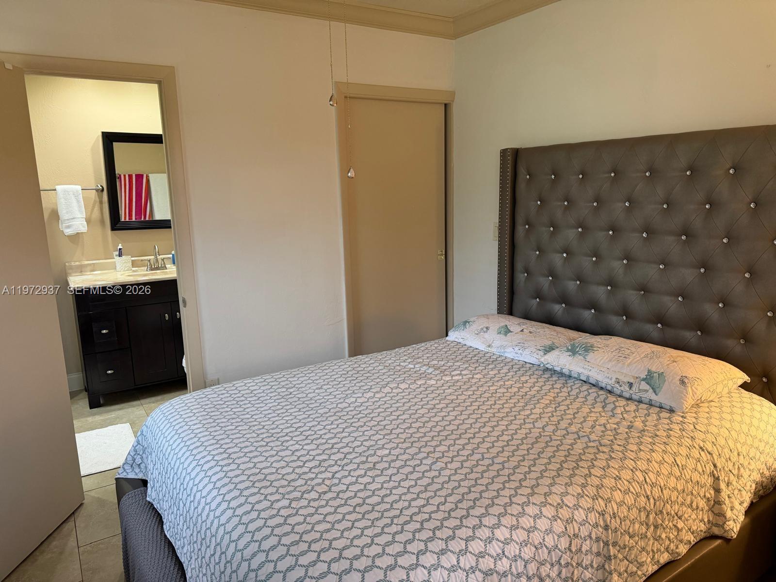 A bedroom features a tufted headboard, patterned bedding, and an adjacent bathroom with a vanity — 1350 NW 96th St # 2, Miami FL 33147, MIAMI, FL