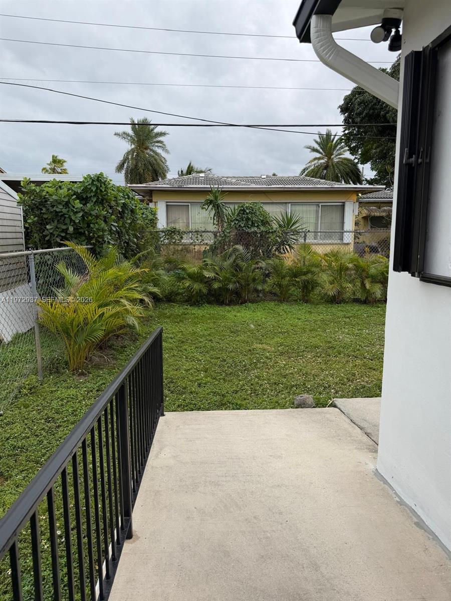 A concrete patio overlooks a grassy backyard with palm trees and a neighboring house — 1350 NW 96th St # 2, Miami FL 33147, MIAMI, FL