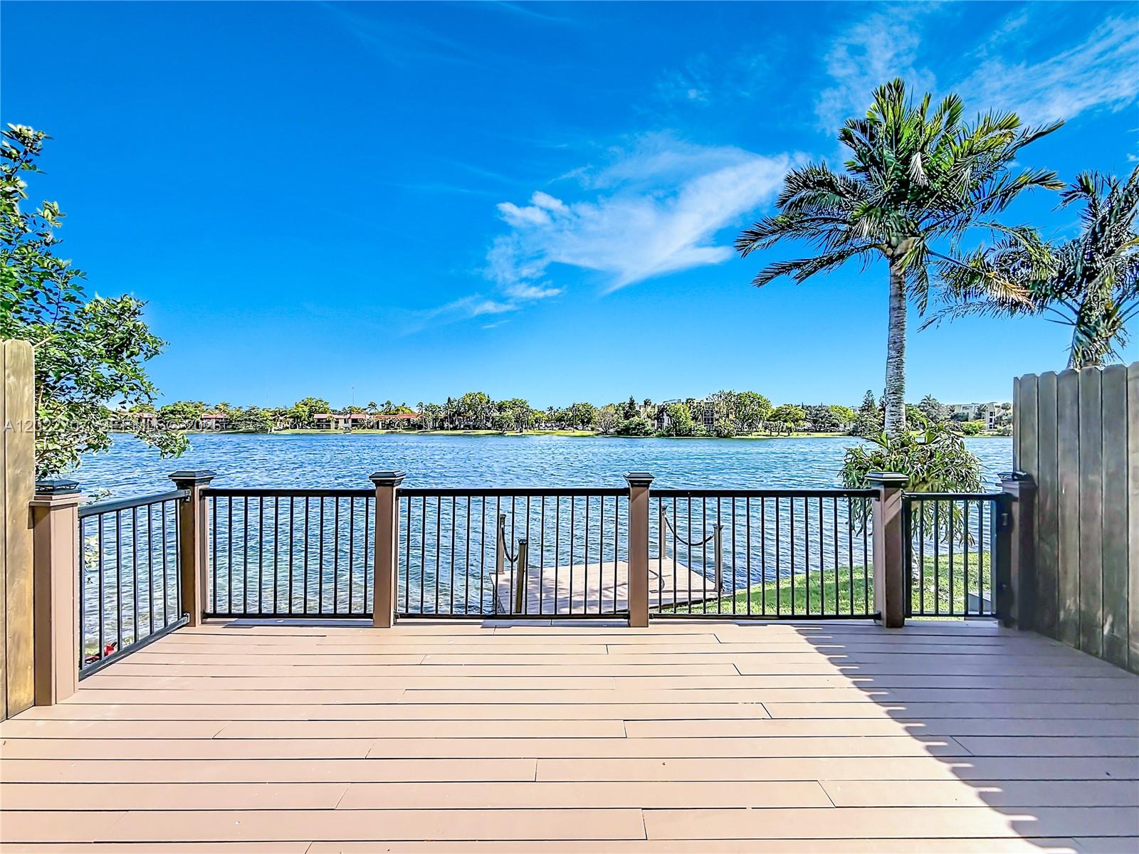 A wooden deck overlooks a lake with a small dock and a palm tree — 781 NE 195th St, Miami FL 33179, MIAMI, FL
