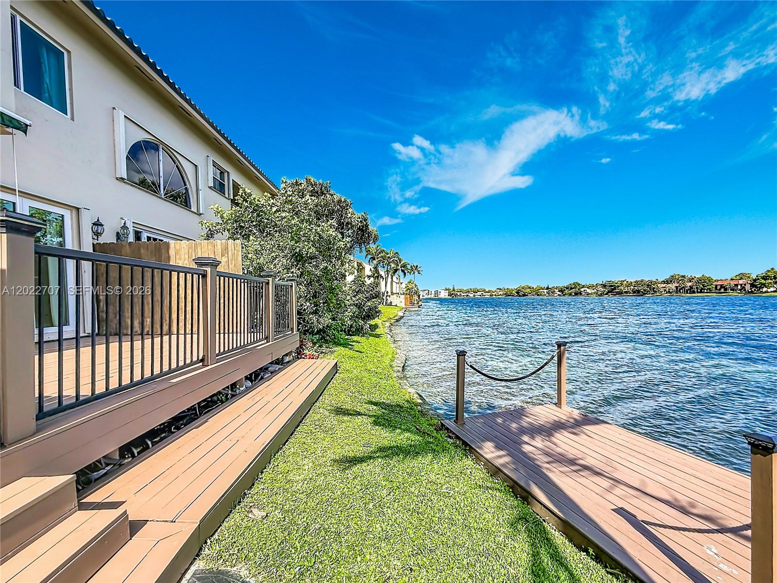 A wooden deck and private dock overlook a lake behind a multi-story residential building — 781 NE 195th St, Miami FL 33179, MIAMI, FL