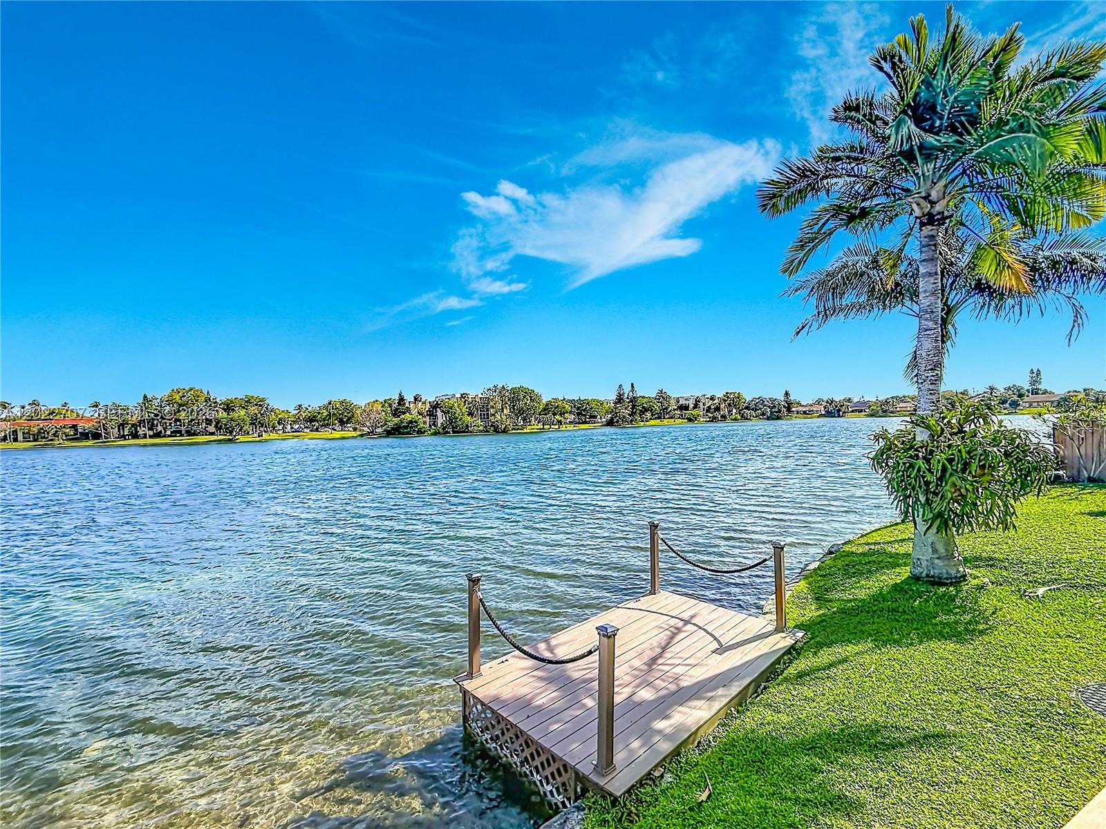 A wooden dock with rope railings sits on the grassy shore of a lake — 781 NE 195th St, Miami FL 33179, MIAMI, FL