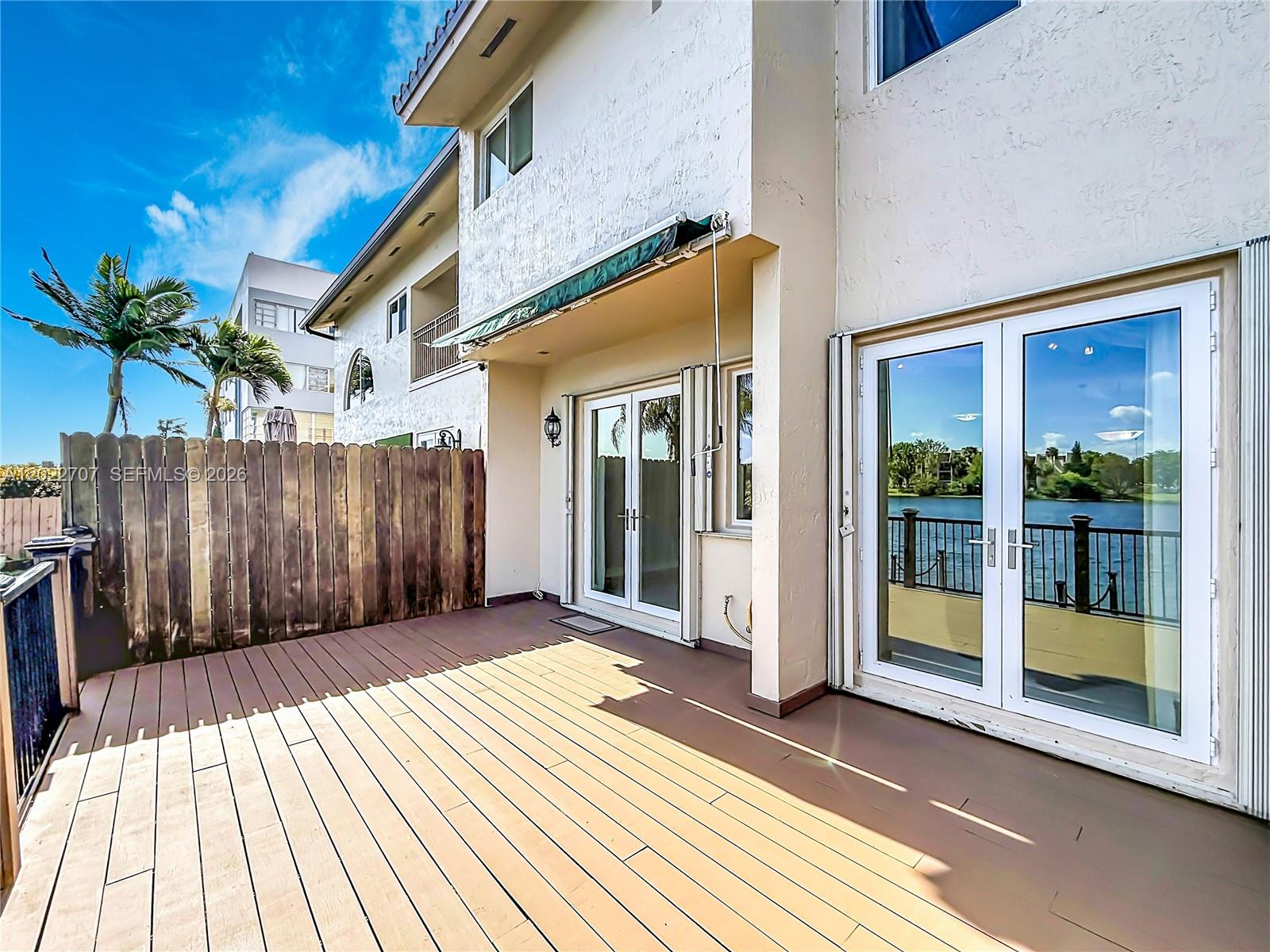 A wooden deck leads to glass double doors overlooking a body of water — 781 NE 195th St, Miami FL 33179, MIAMI, FL