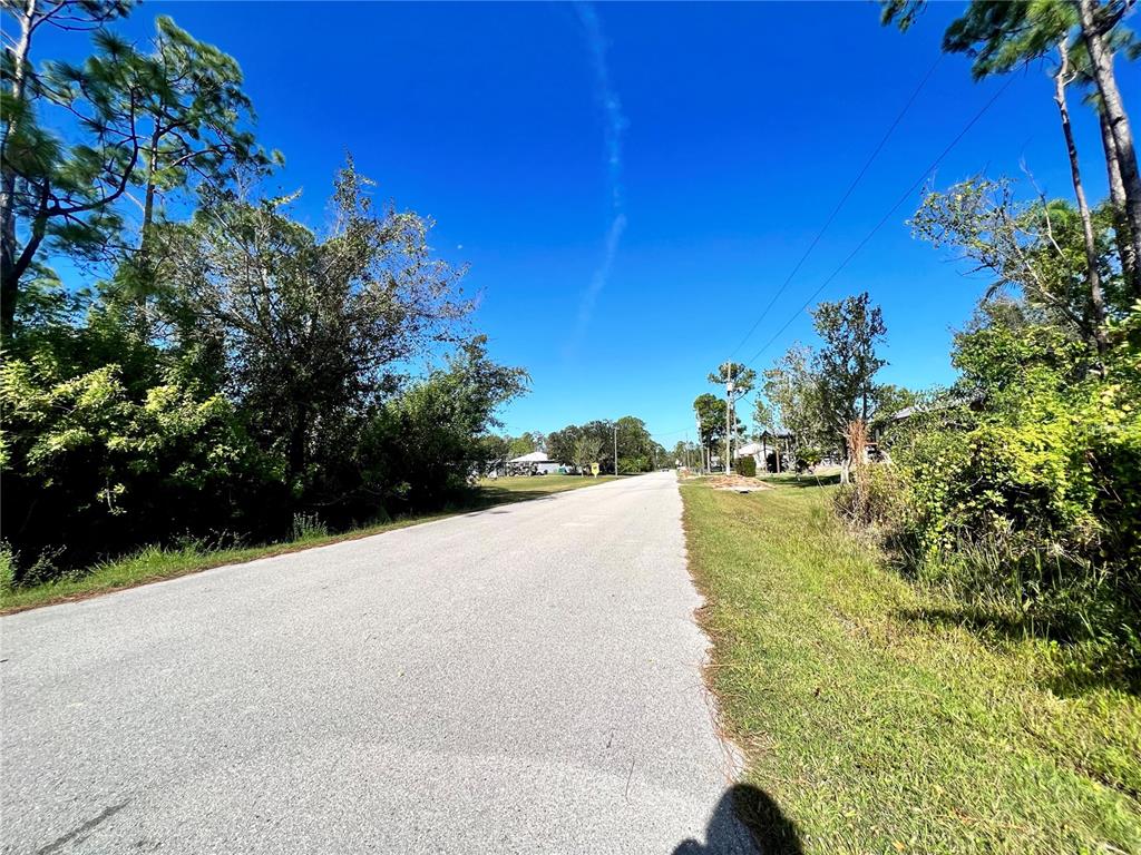 A paved road stretches into the distance, flanked by trees and grassy areas under a sky — 12338 CATALINA DRIVE, PUNTA GORDA, FL