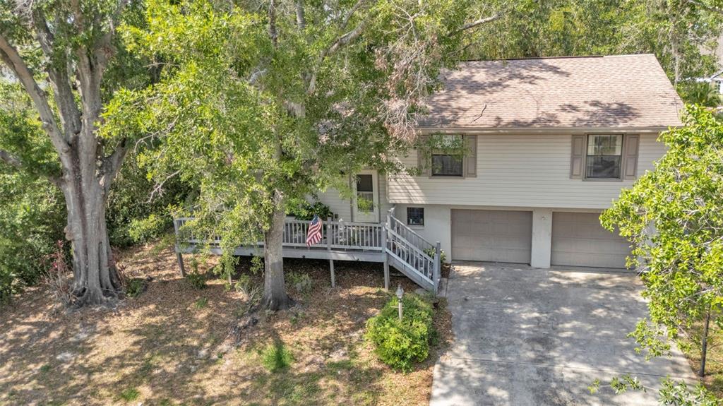 An elevated two-story house with a wooden deck, two garage doors, and surrounding trees — 5324 LAFAYETTE AVENUE, SEBRING, FL