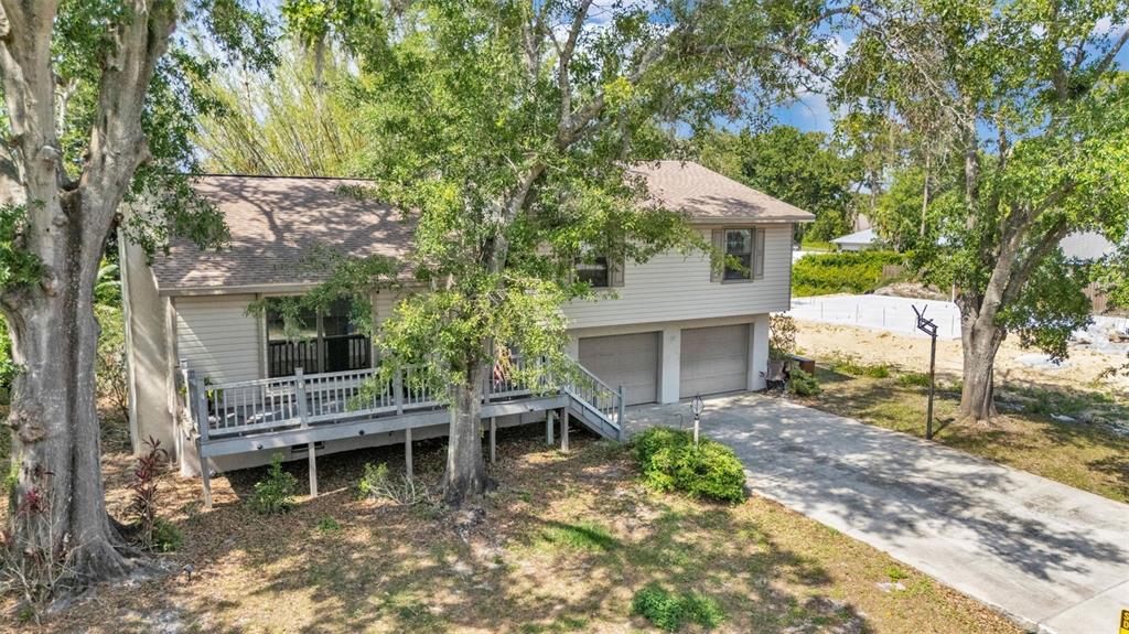 An elevated two-story house with a wooden deck, two garage doors, and surrounding trees — 5324 LAFAYETTE AVENUE, SEBRING, FL