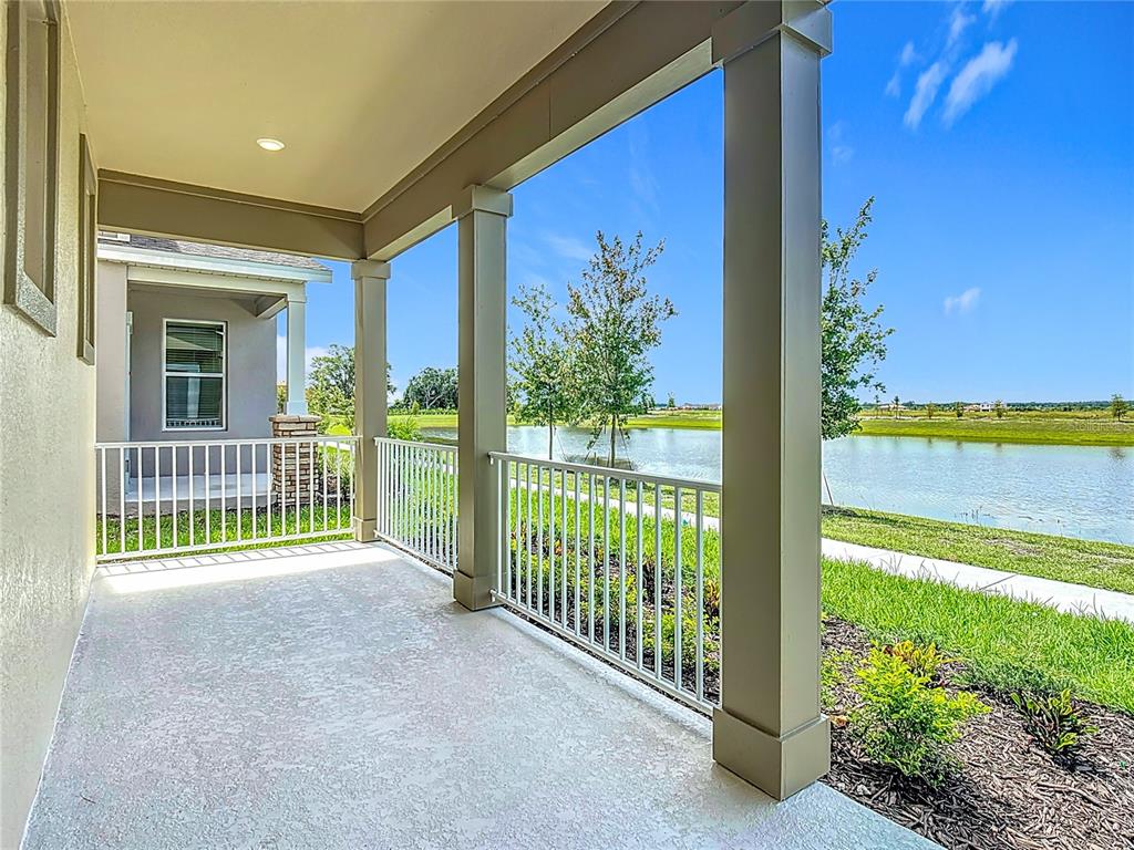 A covered porch with white railings overlooks a pond and grassy landscape — 2433 SPRING TUNE ALLEY, KISSIMMEE, FL