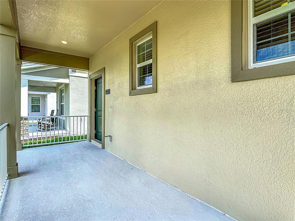 A covered balcony features a beige stucco wall, a dark-framed door, and a metal railing — 2433 SPRING TUNE ALLEY, KISSIMMEE, FL