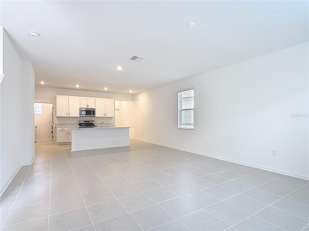 An open-concept kitchen with white cabinets and a center island overlooks a tiled living area — 2433 SPRING TUNE ALLEY, KISSIMMEE, FL
