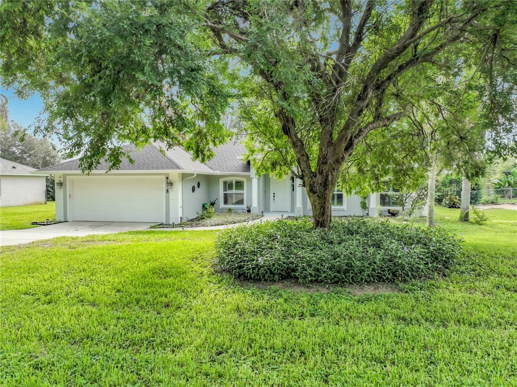 A single-story house with a white garage and a large tree in the front yard — 9418 MEADOW CREST LANE, CLERMONT, FL