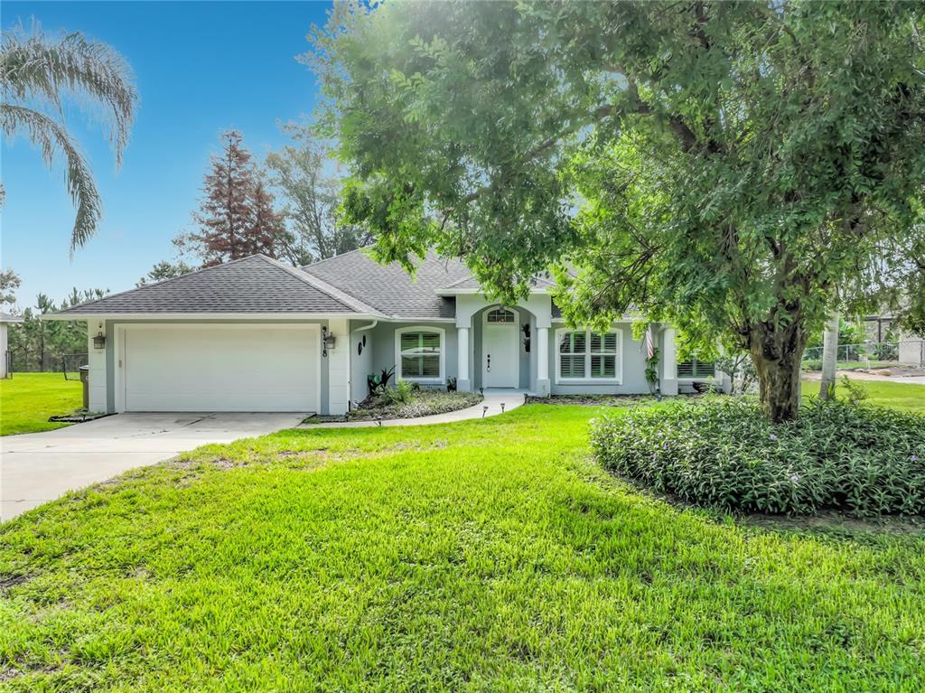 A single-story house with a white garage, gray exterior, and a large tree in front — 9418 MEADOW CREST LANE, CLERMONT, FL