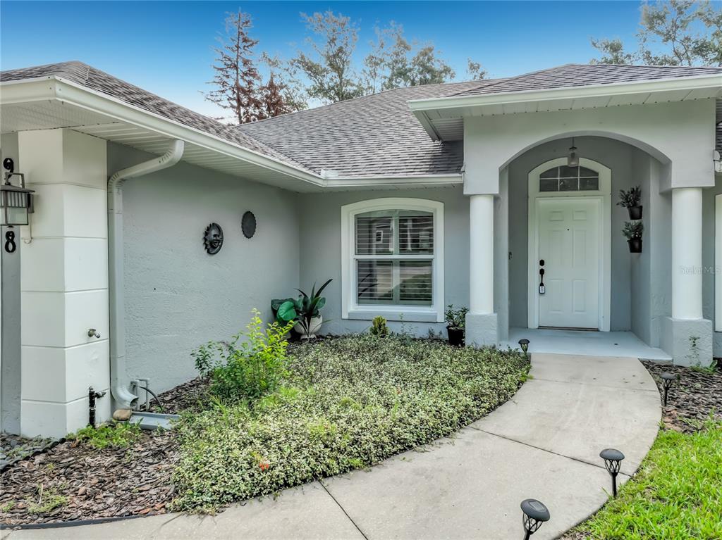 The exterior of a single-story house features a gray stucco facade, arched entryway, and walkway — 9418 MEADOW CREST LANE, CLERMONT, FL