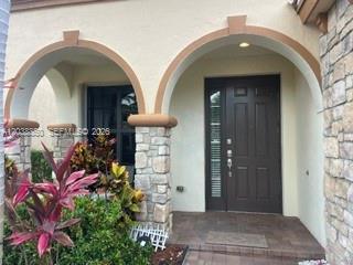 A dark wood front door sits between two stone-clad arched entryways on a paved porch — 3837 Aspen Leaf Dr, Boynton Beach FL 33436, BOYNTON BEACH, FL