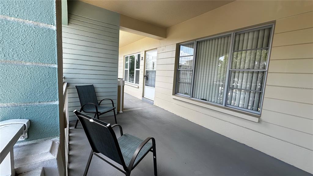 A covered outdoor balcony features two chairs, light-colored siding, and a glass-paned entry door — 2330 ECUADORIAN WAY UNIT 32, CLEARWATER, FL